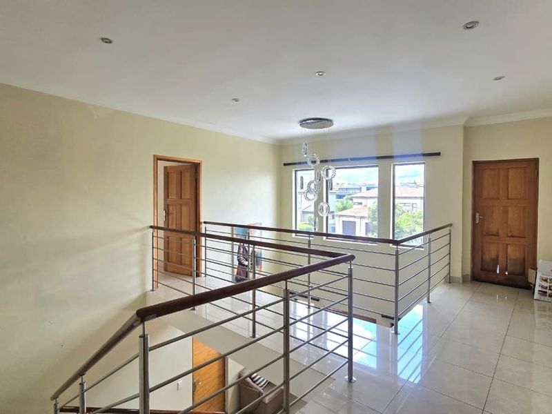 A spacious upper-level landing area featuring tiled flooring, a modern stainless steel balustrade with a wooden handrail, and access to multiple rooms.