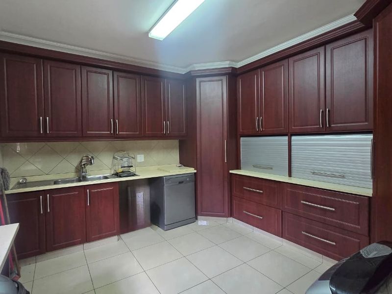 A functional kitchen featuring dark wood cabinetry, ample storage with roller shutter appliance garages, tiled backsplash, and integrated dishwasher.
