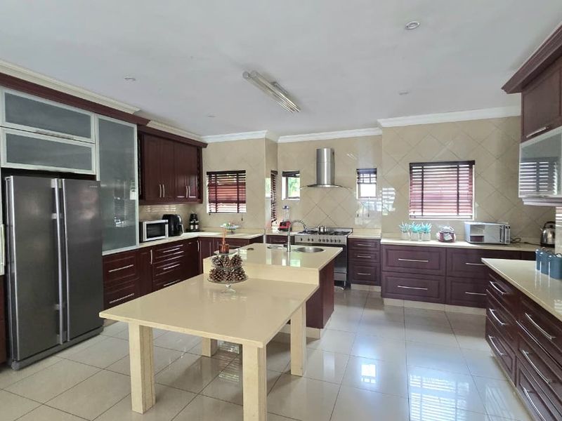Spacious kitchen featuring dark wood cabinetry, stone countertops, a central island, stainless steel appliances, and tiled flooring throughout.