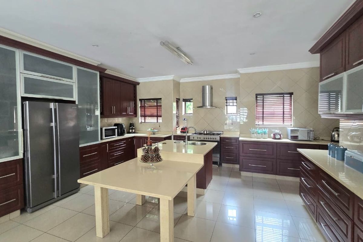 Spacious kitchen featuring dark wood cabinetry, stone countertops, a central island, stainless steel appliances, and tiled flooring throughout.