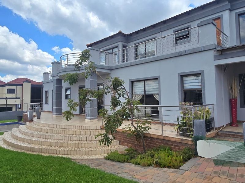 Rear view of a double-story residence featuring a tiled patio, upper-level balcony with stainless steel railings, and an adjacent swimming pool.