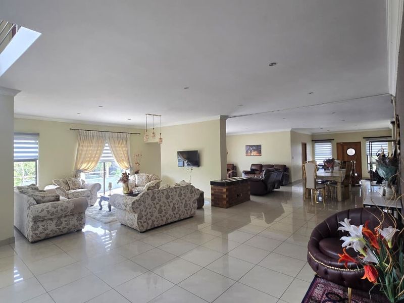 Spacious open-plan living and dining area featuring large format floor tiles, recessed lighting, and a double-volume ceiling height.
