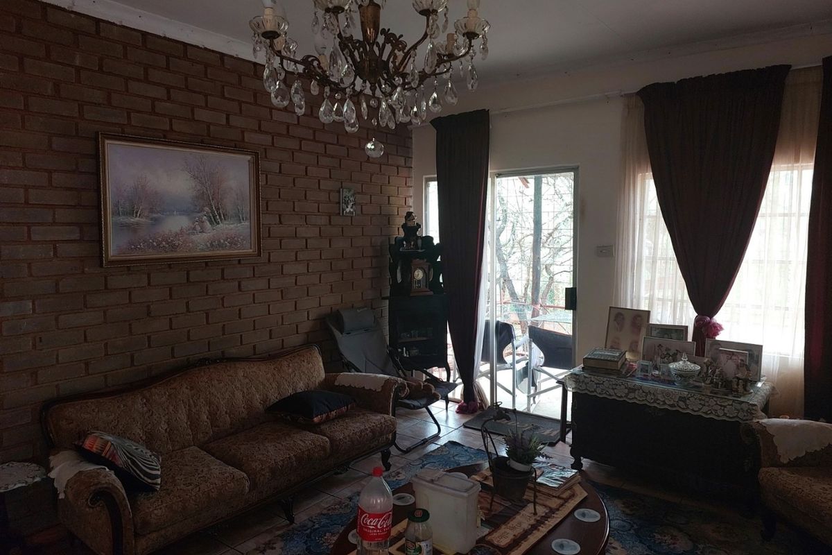 A living room featuring an exposed brick wall, tiled flooring, and a crystal chandelier, with direct access to an outdoor area via a sliding door.