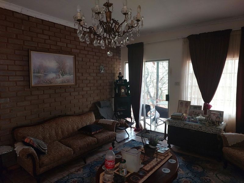 A living room featuring an exposed brick wall, tiled flooring, and a crystal chandelier, with direct access to an outdoor area via a sliding door.