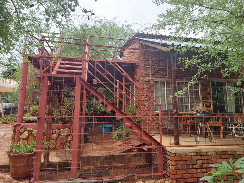 Rear exterior view of a rustic brick farmhouse featuring a covered patio area and an external metal staircase enclosed by security fencing.