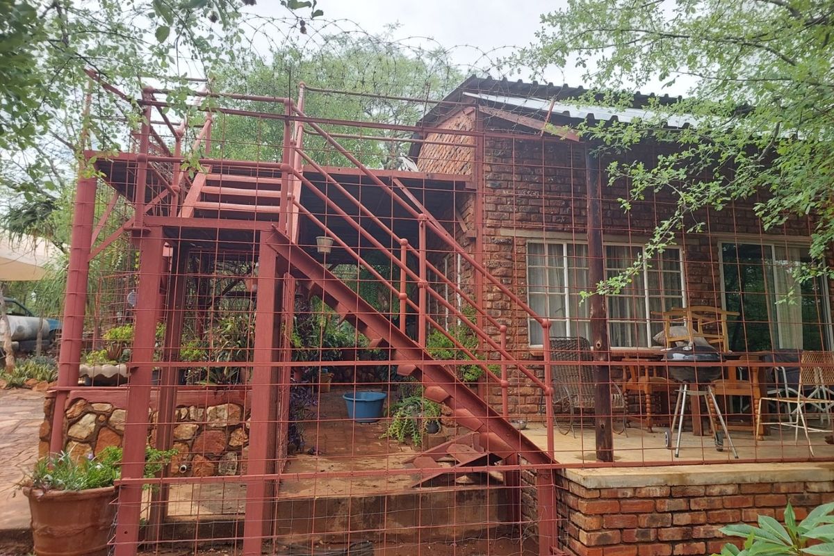 Rear exterior view of a rustic brick farmhouse featuring a covered patio area and an external metal staircase enclosed by security fencing.