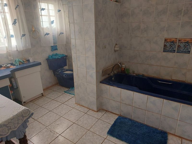 A dated bathroom featuring blue sanitaryware, tiled walls, a built-in bathtub, and a vanity cabinet. The space requires modernization of finishes and fixtures.