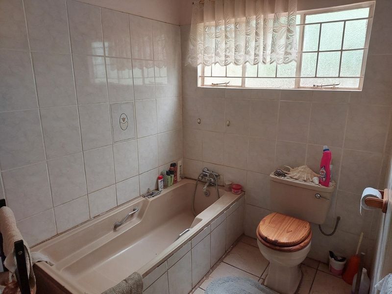 A dated bathroom featuring a built-in bathtub, ceramic wall and floor tiles, and a standard toilet with a window providing natural light.