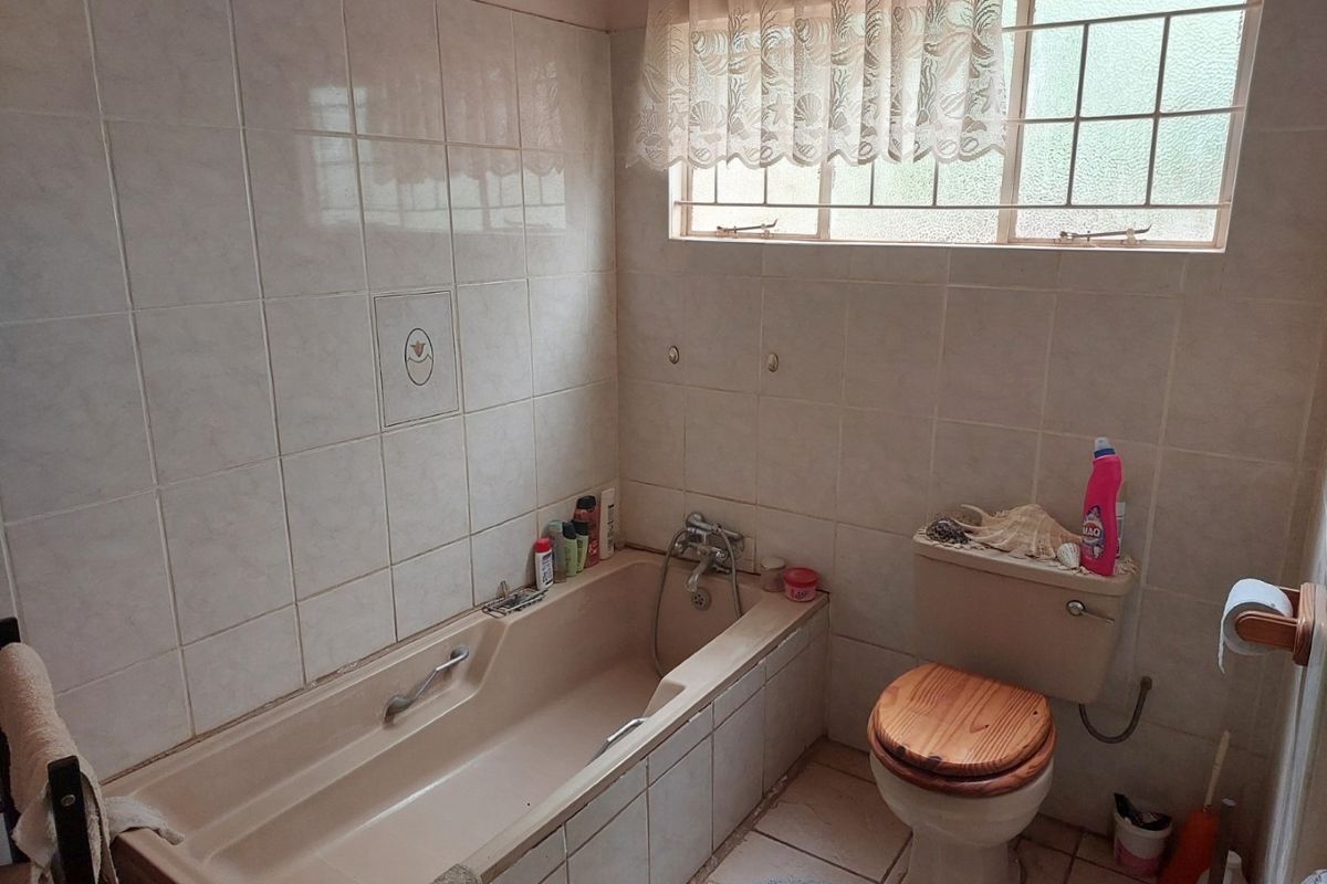 A dated bathroom featuring a built-in bathtub, ceramic wall and floor tiles, and a standard toilet with a window providing natural light.