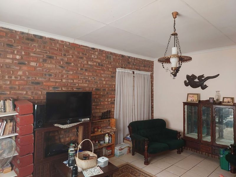 Living room featuring an exposed brick wall, tiled flooring, and a vintage pendant light fixture, requiring some ceiling maintenance.