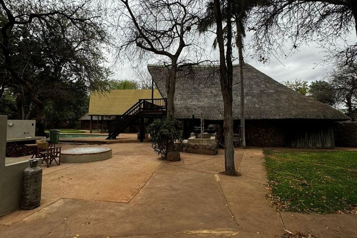 Rear exterior view of a farm-style property featuring a large thatched roof, concrete patio area, outdoor staircase, and swimming pool.
