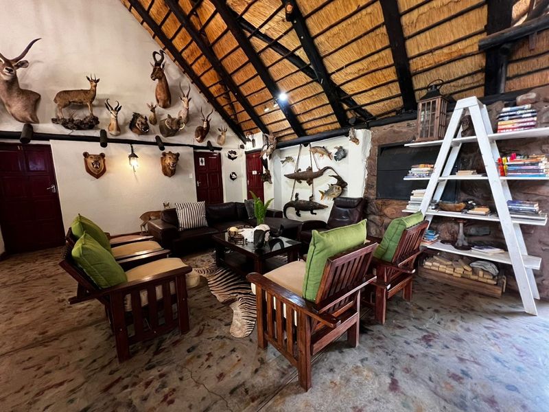 Rustic living room featuring a high vaulted thatched roof with exposed timber rafters, stone fireplace, and durable concrete flooring.