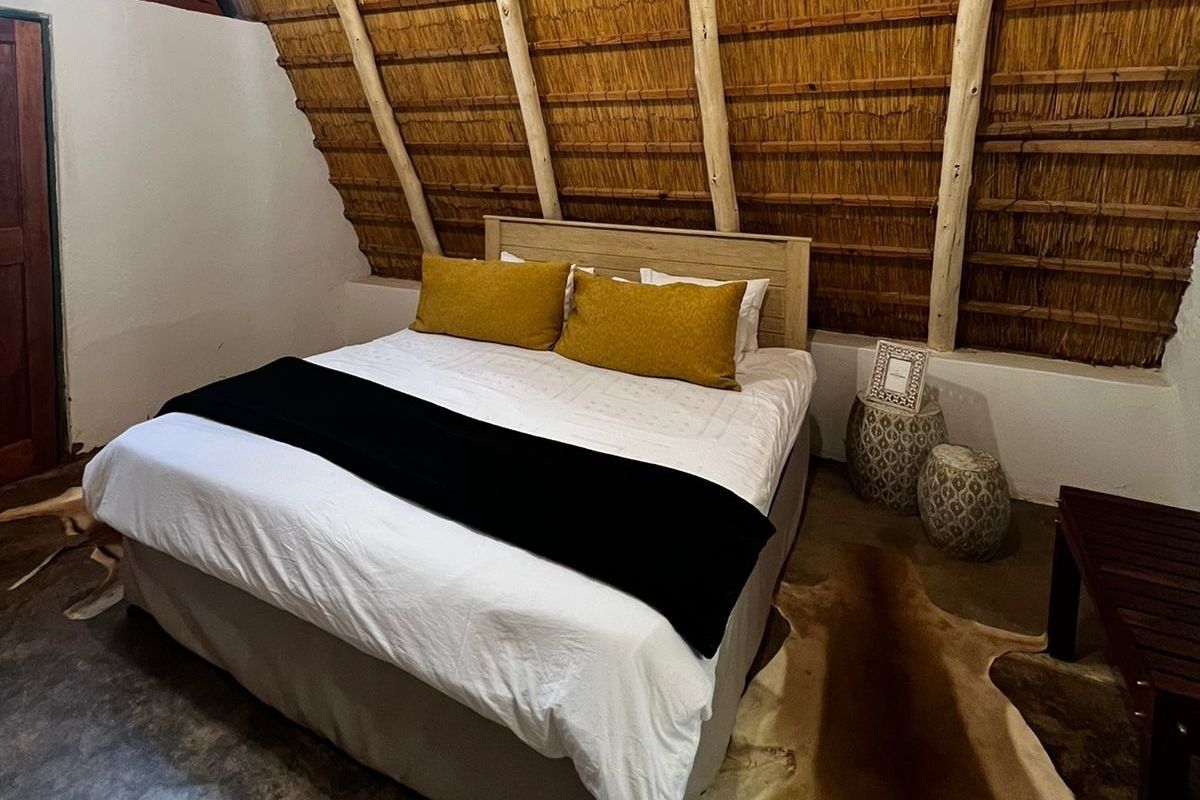 A cozy bedroom featuring a unique thatched roof with exposed timber rafters and durable concrete flooring, creating a rustic farm-style atmosphere.