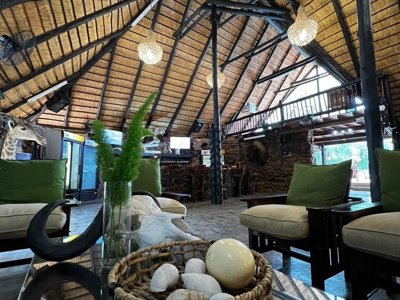 Spacious rustic bar area featuring a high thatched roof with exposed timber trusses, stone walls, and a mezzanine level overlooking the main space.