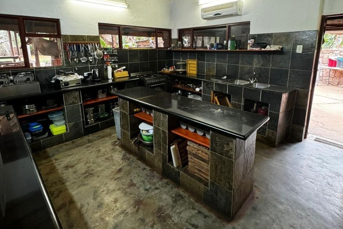 A rustic kitchen featuring stone-tiled cabinetry, a central island, double basin sink, and built-in stove, offering a functional workspace with a farm-style aesthetic.