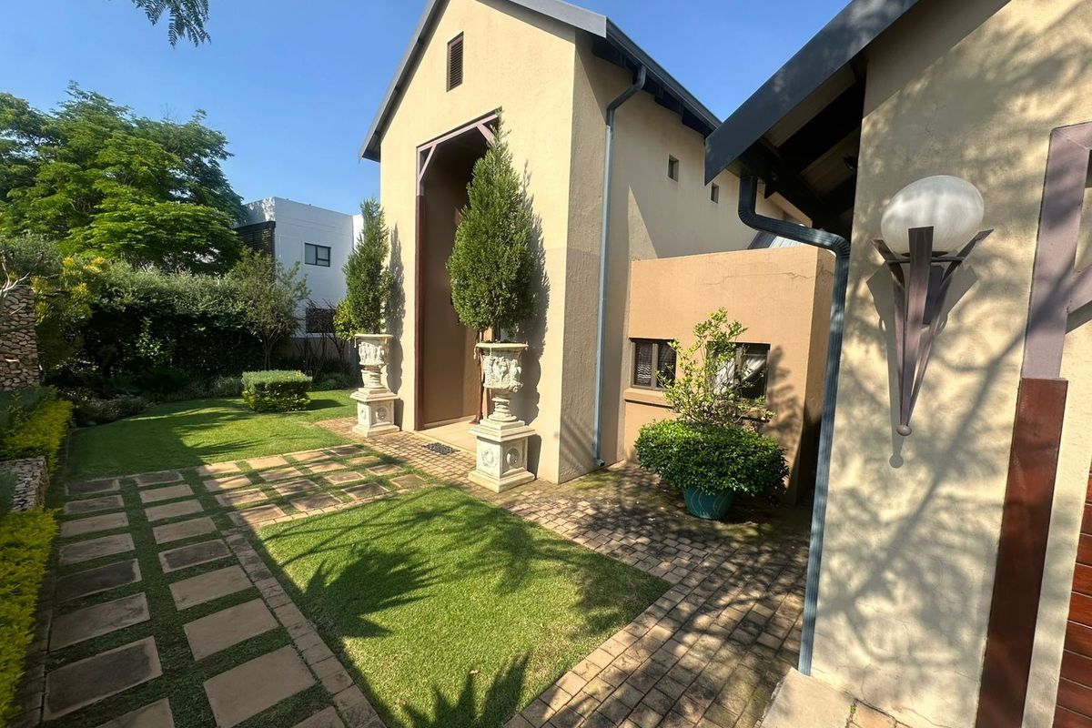 A well-maintained rear garden area featuring a paved walkway, manicured lawn, and established landscaping alongside the building exterior.