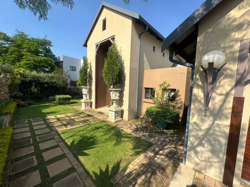 A well-maintained rear garden area featuring a paved walkway, manicured lawn, and established landscaping alongside the building exterior.