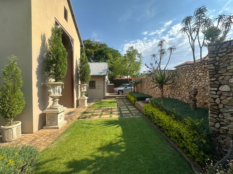 A well-maintained rear garden featuring a stone boundary wall, manicured lawn, and paved walkway leading towards the side of the property.