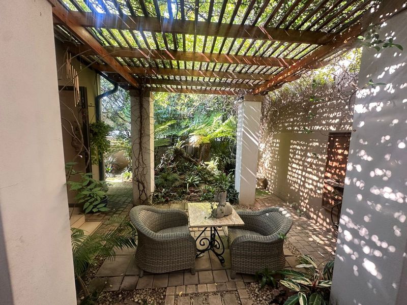 A charming covered patio area featuring a timber pergola and paved flooring, overlooking a lush, landscaped garden setting.