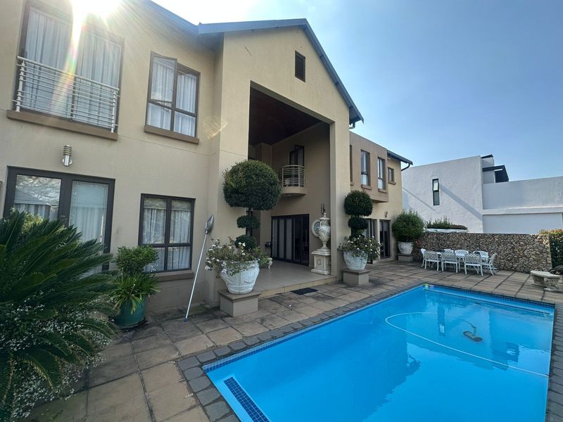 Rear exterior view featuring a swimming pool, paved patio area, and a multi-story building facade with a balcony.