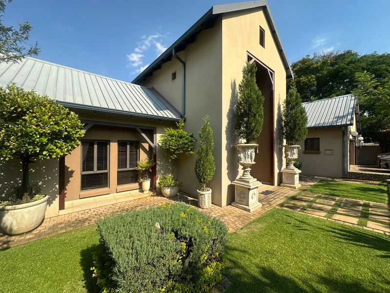 A well-maintained front entrance featuring a striking architectural facade, metal roofing, and neatly landscaped garden with paved pathways.