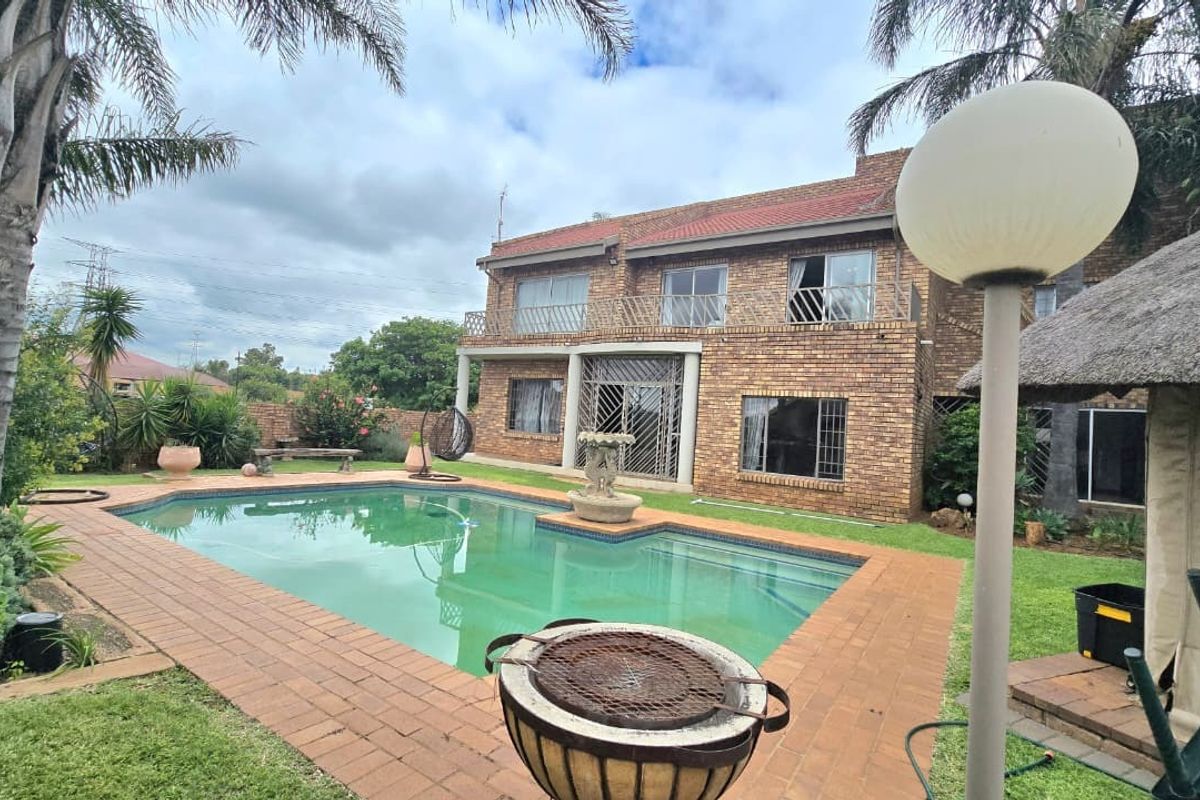 Rear view of a double-story brick house featuring a swimming pool, paved patio area, and a thatched lapa in the garden.