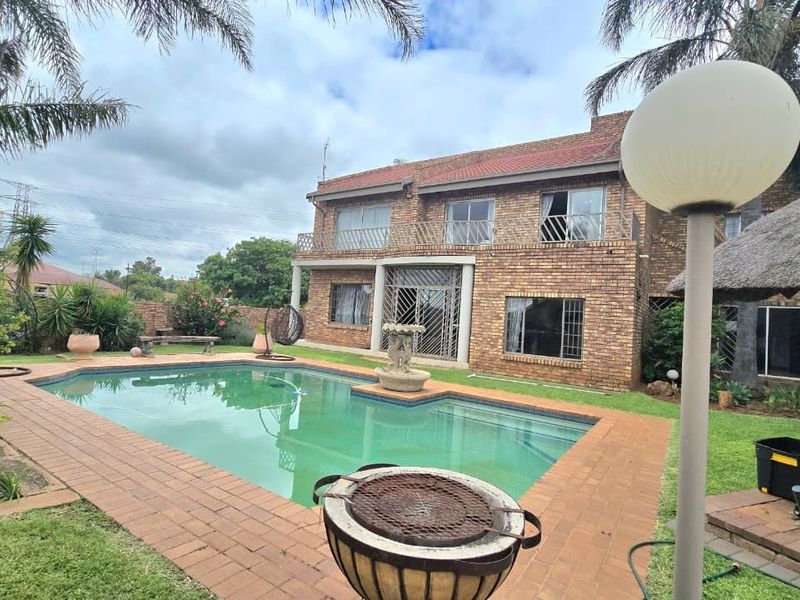 Rear view of a double-story brick house featuring a swimming pool, paved patio area, and a thatched lapa in the garden.