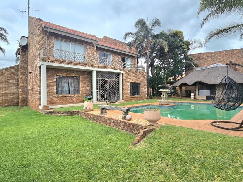 Rear view of a double-story brick house featuring a swimming pool, a thatched lapa, and a spacious garden area.