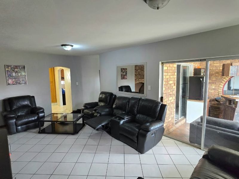 Spacious living room featuring tiled flooring, an exposed brick feature wall, and a large sliding glass door providing access to the outdoor area.