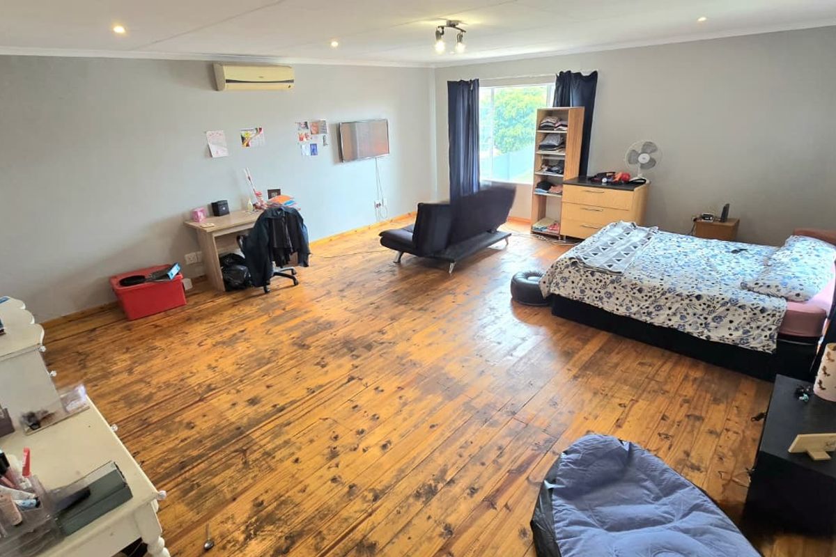 Spacious bedroom featuring polished timber flooring, recessed downlighting, and a wall-mounted air conditioning unit.