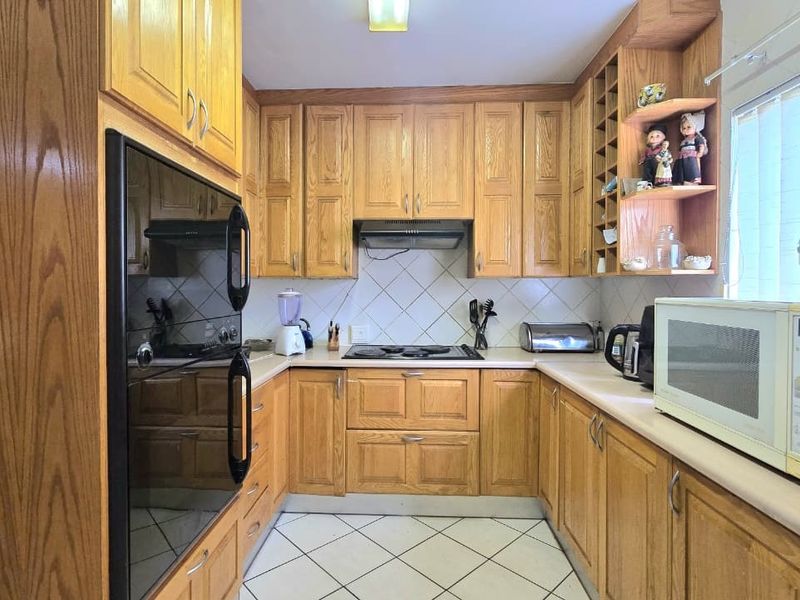 A functional U-shaped kitchen featuring traditional oak cabinetry, built-in oven, electric hob, and tiled finishes, offering a classic layout with ample storage space.