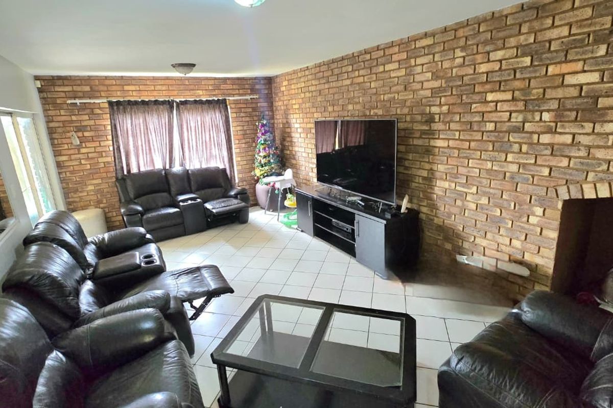 Spacious living room featuring a prominent exposed brick wall, tiled flooring, and a built-in fireplace, offering a warm and textured aesthetic.