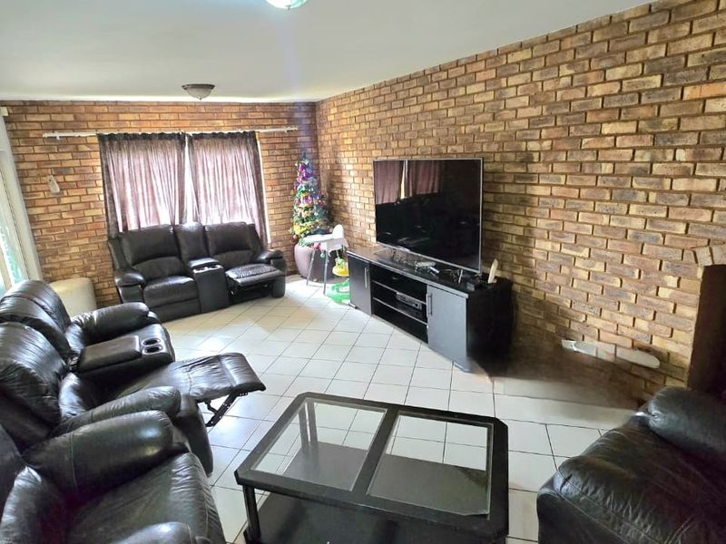 Spacious living room featuring a prominent exposed brick wall, tiled flooring, and a built-in fireplace, offering a warm and textured aesthetic.