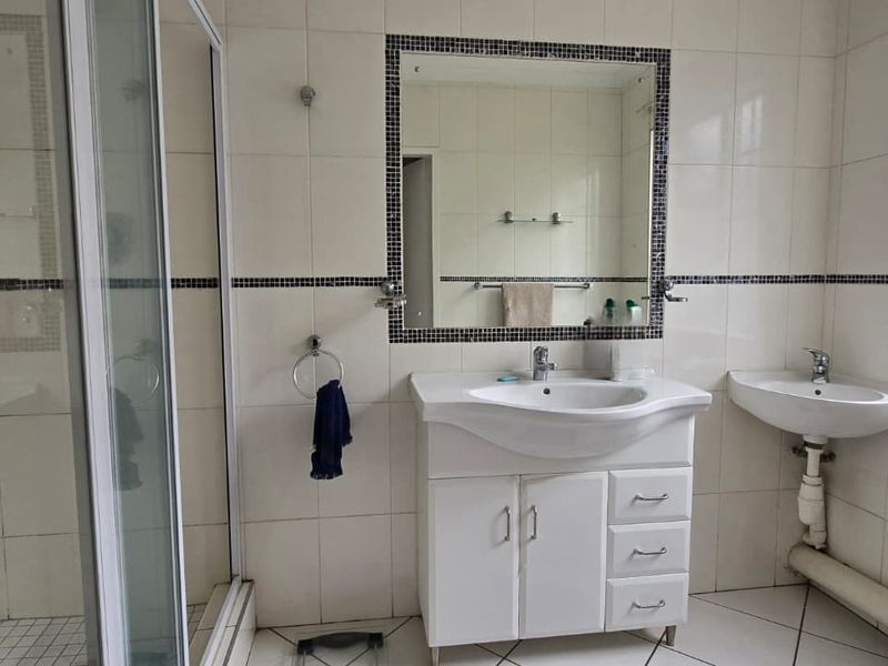 A functional bathroom featuring a shower enclosure, vanity cabinet with basin, additional wall-mounted basin, and tiled finishes throughout.