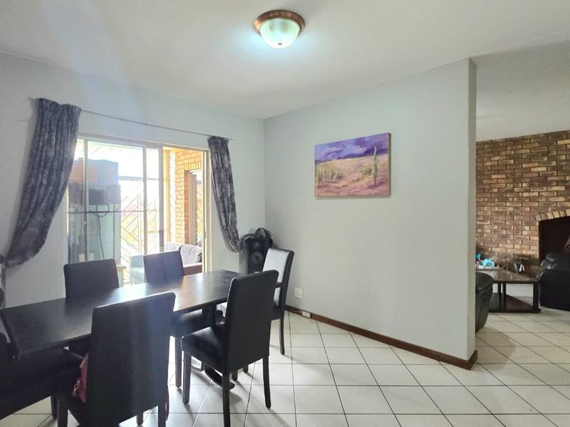 Open plan dining area featuring tiled flooring, a sliding door to the patio, and an adjacent living space with a prominent brick fireplace.