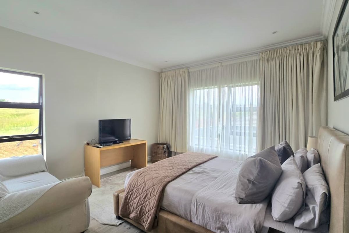 A well-lit bedroom featuring neutral walls, recessed downlighting, and large windows with floor-to-ceiling curtains providing ample natural light.