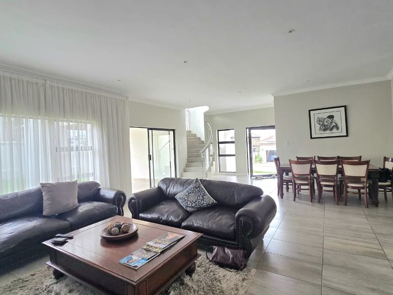 Spacious open-plan living and dining area featuring large format floor tiles, recessed lighting, and a feature staircase leading to the upper level.