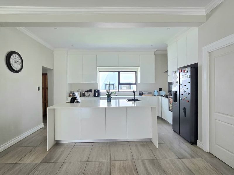 Modern kitchen featuring a central island, sleek white cabinetry, stone countertops, and neutral tiled flooring, offering a clean and functional culinary space.