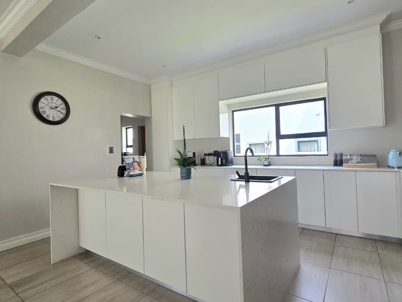 Modern kitchen featuring a large central island with quartz countertops, sleek white cabinetry, and tiled flooring in a bright, open-plan layout.