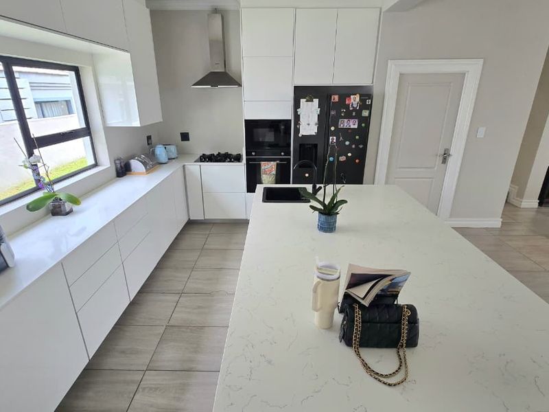 Modern kitchen featuring white cabinetry, quartz countertops, a central island with an integrated sink, and high-quality built-in appliances.