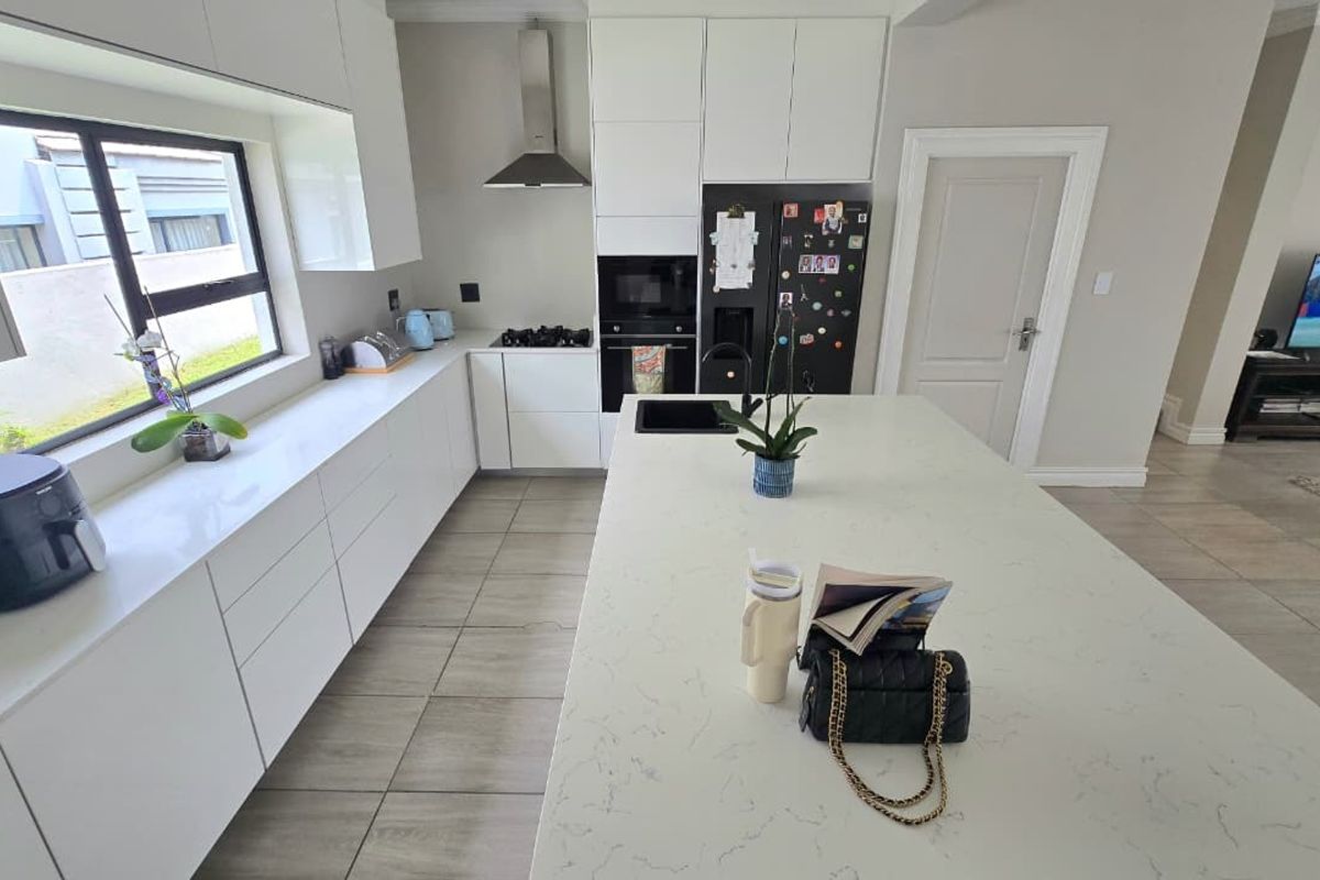 Modern kitchen featuring white cabinetry, quartz countertops, a central island with an integrated sink, and high-quality built-in appliances.