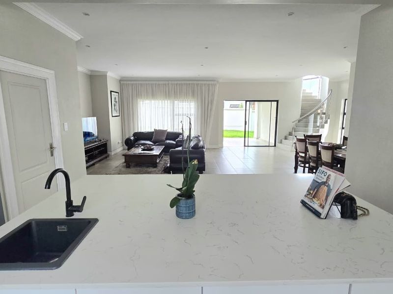Spacious open-plan living area featuring a modern kitchen island with quartz countertops, flowing seamlessly into the dining and lounge spaces with garden access.