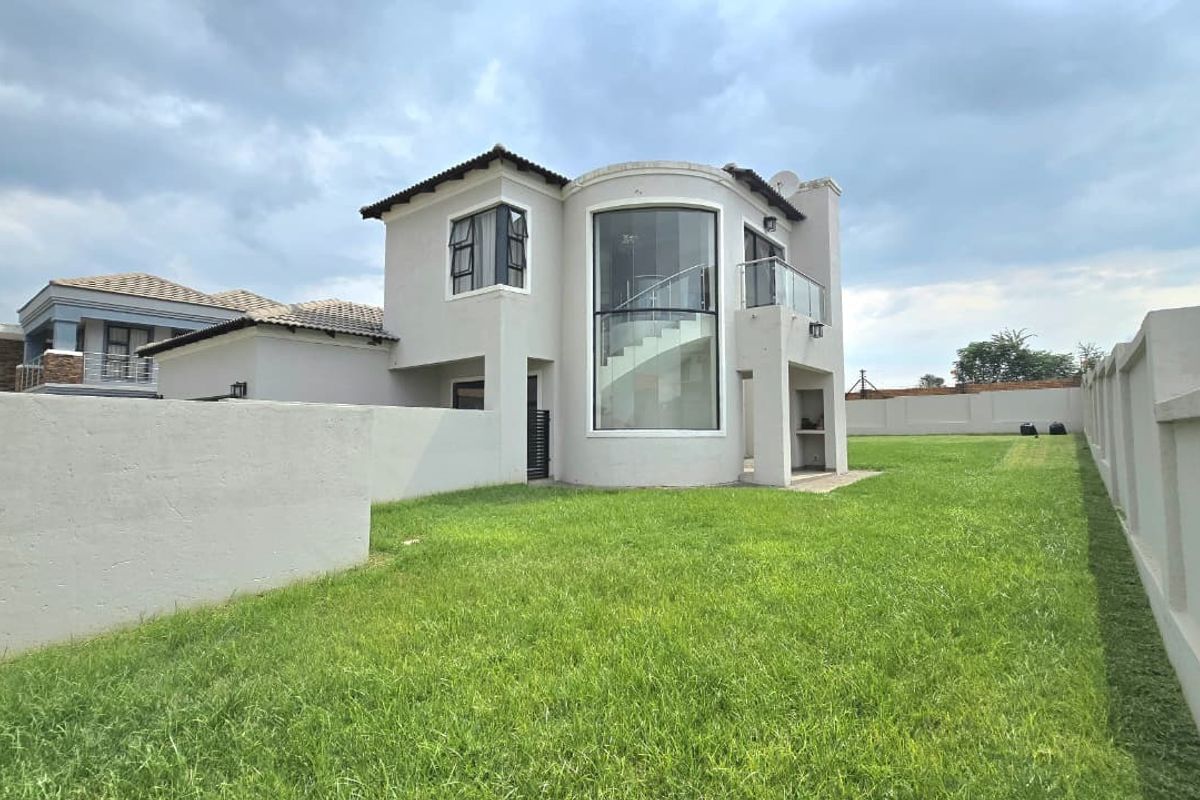 Rear view of a modern double-story house featuring a curved glass facade, a balcony with glass balustrades, and a spacious private garden.