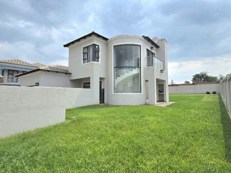 Rear view of a modern double-story house featuring a curved glass facade, a balcony with glass balustrades, and a spacious private garden.