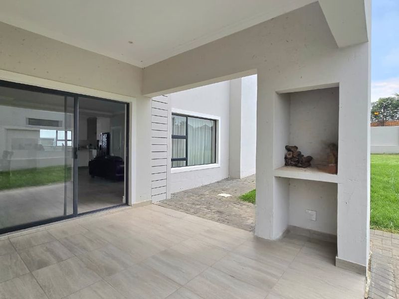 A covered patio featuring tiled flooring, a built-in braai, and sliding glass doors providing access to the interior living space.
