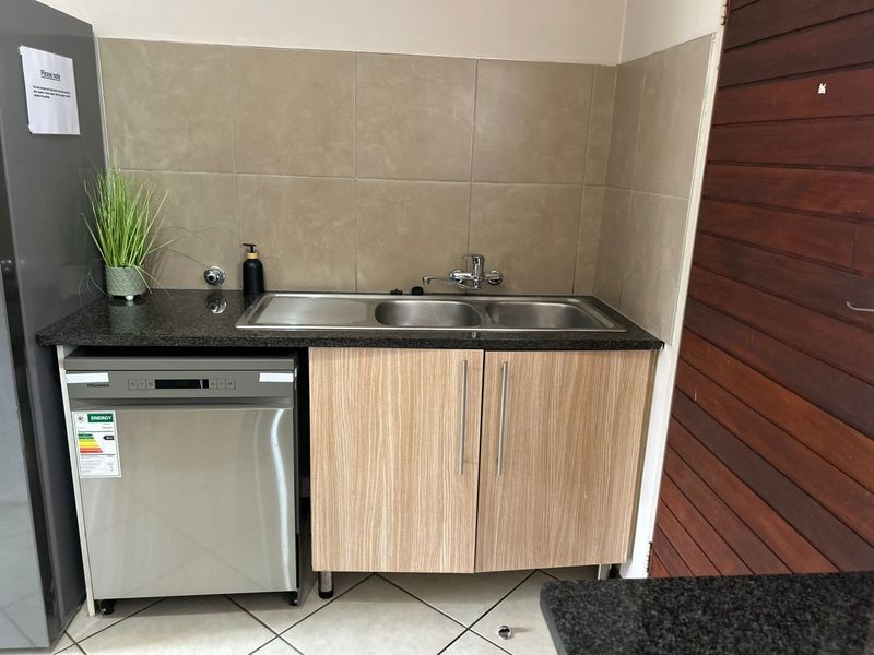 A functional scullery area featuring a double sink, granite countertops, laminate cabinetry, and tiled splashback, providing practical utility space.