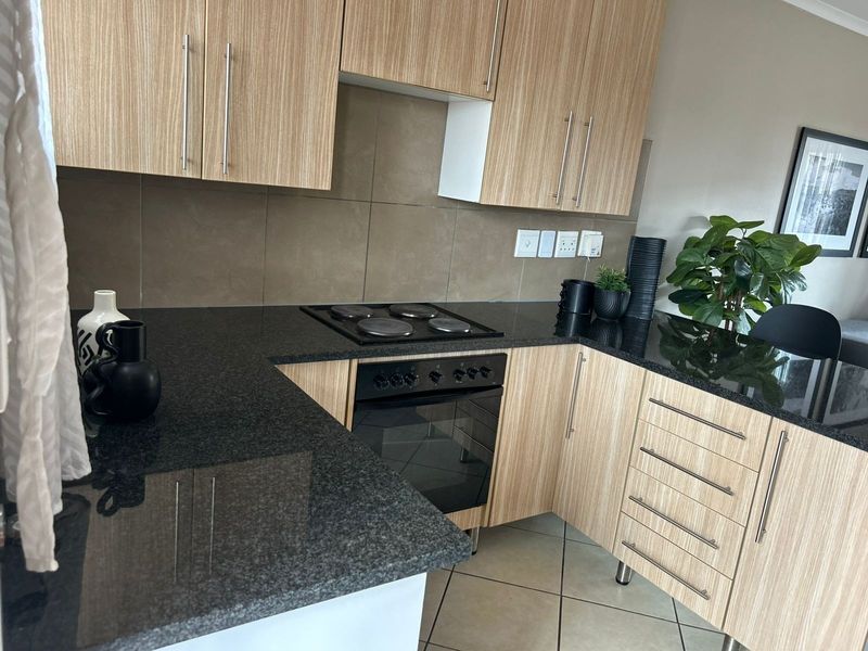 Modern kitchen featuring light wood-grain cabinetry, dark granite countertops, a built-in electric hob and oven, and a neutral tiled backsplash.