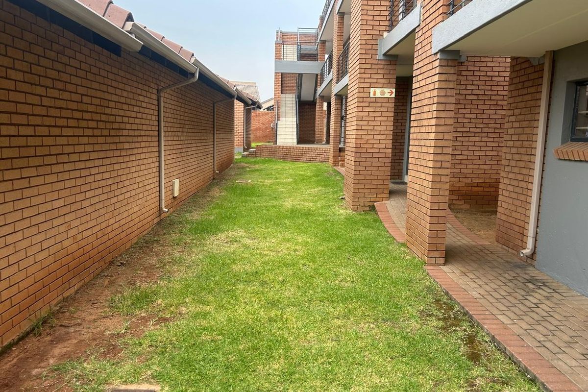 A view of the rear exterior area featuring face brick building facades, a paved walkway, and a lawn between the apartment blocks.