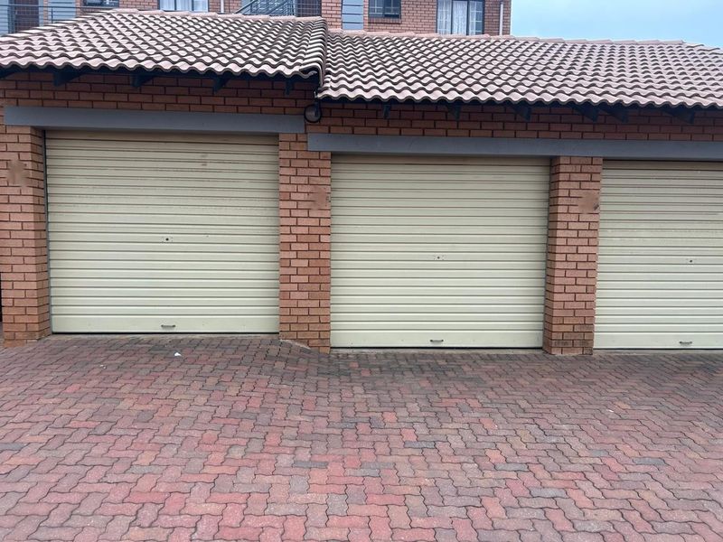 A view of a residential garage block featuring multiple roller shutter doors, brick construction, and a paved driveway.