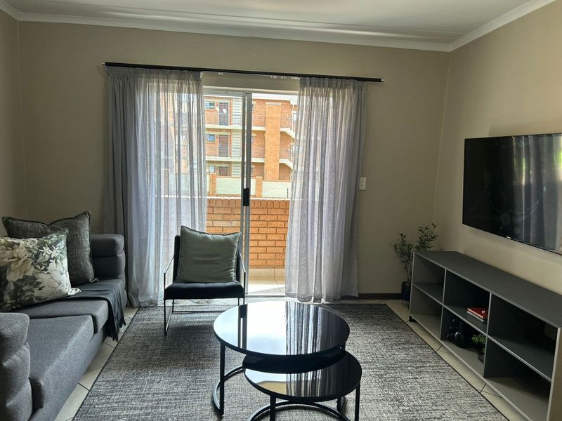 A well-maintained living room featuring tiled flooring, cove cornicing, and a sliding glass door providing access to an outdoor balcony area.